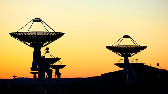 Silhouettes of satellite dishes on a background of orange and yellow